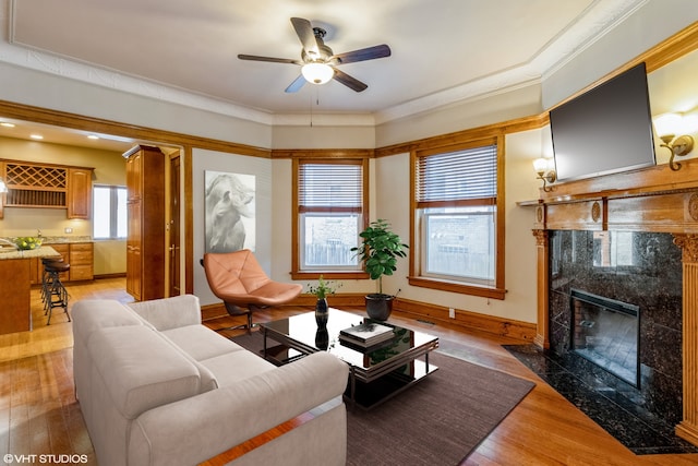 living room with a premium fireplace, light wood-type flooring, ceiling fan, and crown molding