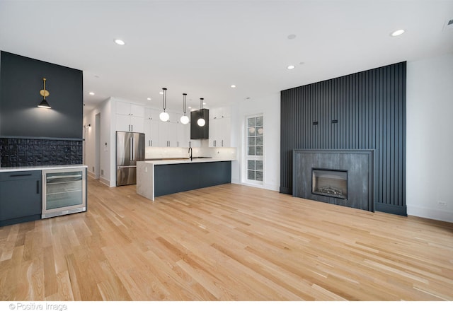 kitchen with light wood-type flooring, wine cooler, white cabinetry, hanging light fixtures, and stainless steel fridge