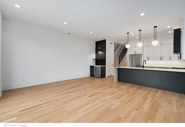 kitchen featuring light hardwood / wood-style floors, white cabinetry, backsplash, stainless steel appliances, and decorative light fixtures