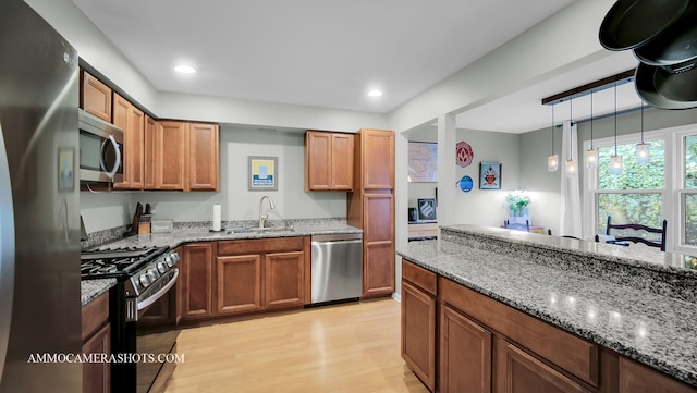 kitchen with sink, decorative light fixtures, stainless steel appliances, light stone countertops, and light hardwood / wood-style floors