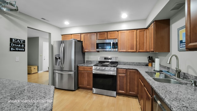 kitchen featuring appliances with stainless steel finishes, light stone countertops, light hardwood / wood-style floors, and sink