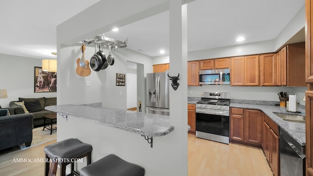 kitchen with appliances with stainless steel finishes, light hardwood / wood-style floors, a breakfast bar area, and light stone counters