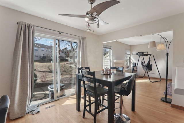 dining area with baseboards, light wood-type flooring, visible vents, and a ceiling fan