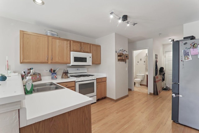 kitchen featuring white appliances, a sink, baseboards, light countertops, and light wood finished floors