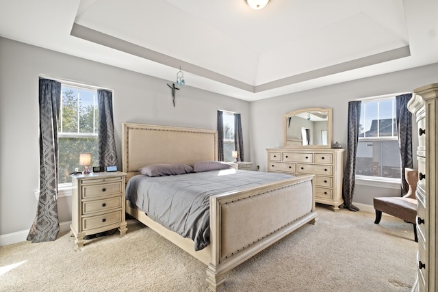 bedroom featuring baseboards, a tray ceiling, light colored carpet, and multiple windows