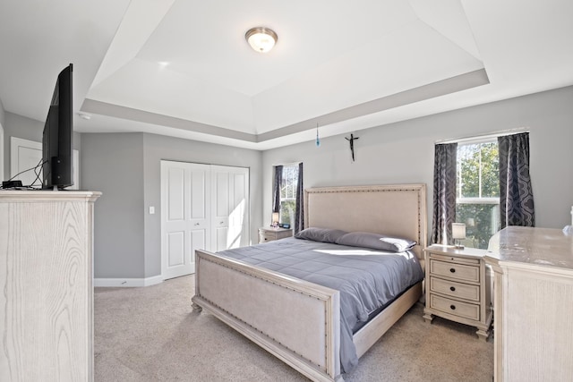 bedroom with light carpet, baseboards, a raised ceiling, and multiple windows