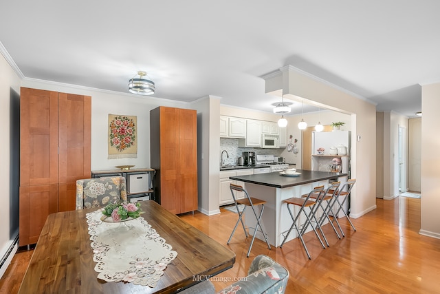 kitchen with white cabinets, ornamental molding, white appliances, light hardwood / wood-style flooring, and a kitchen bar