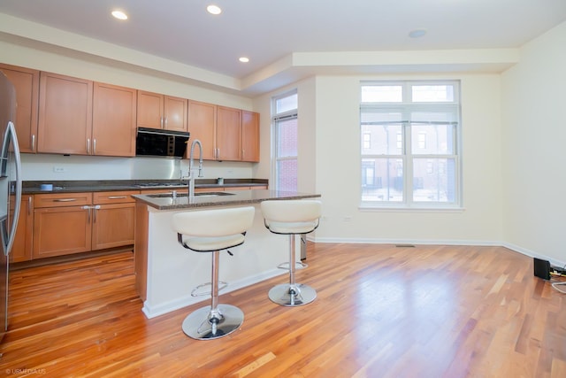 kitchen featuring dark stone countertops, a breakfast bar, an island with sink, and light wood-type flooring