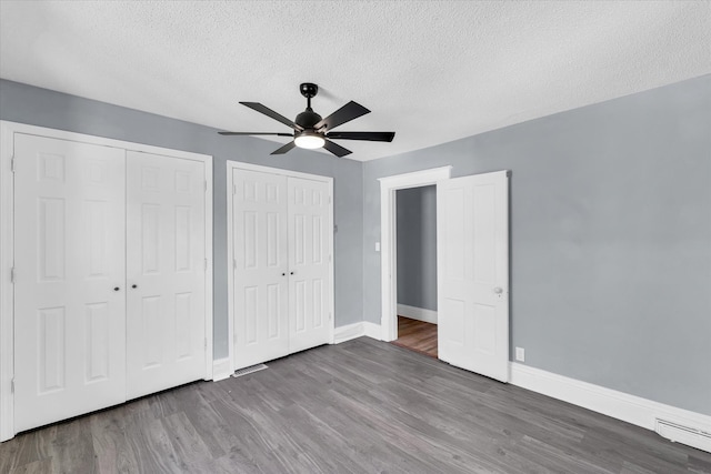 unfurnished bedroom with ceiling fan, a textured ceiling, two closets, and wood-type flooring