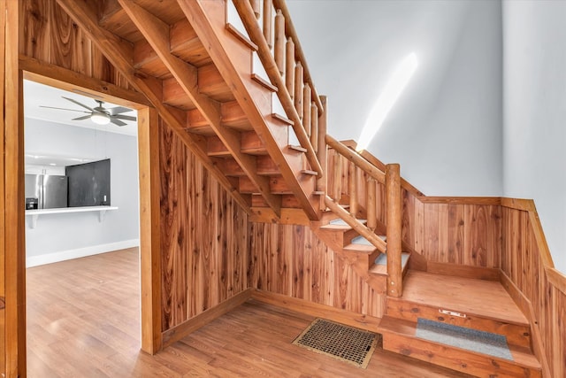 staircase with wood-type flooring, wood walls, and ceiling fan