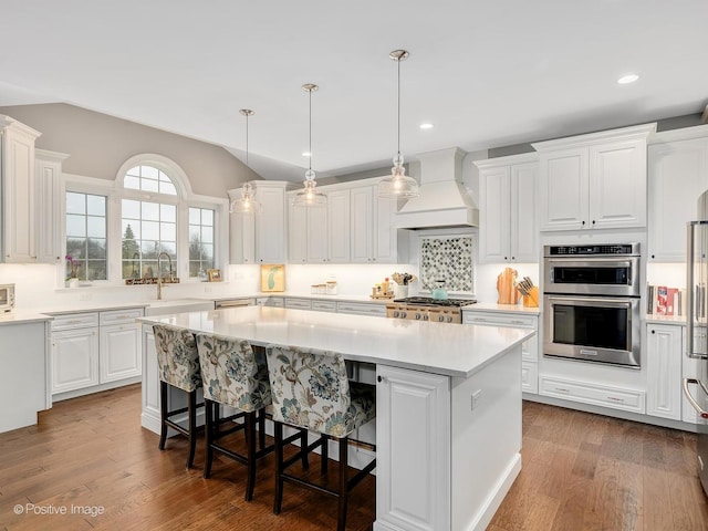 kitchen featuring premium range hood, a center island, hanging light fixtures, stainless steel double oven, and white cabinets