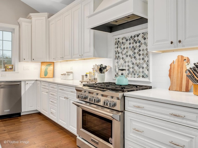 kitchen with backsplash, stainless steel appliances, custom range hood, white cabinets, and light wood-type flooring