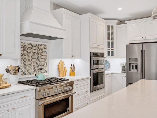 kitchen with premium range hood, appliances with stainless steel finishes, decorative backsplash, and white cabinets