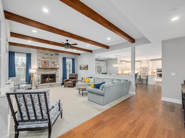 living room featuring ceiling fan, a stone fireplace, beamed ceiling, and hardwood / wood-style flooring