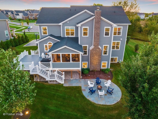 back house at dusk with a deck, a lawn, a patio area, and an outdoor fire pit