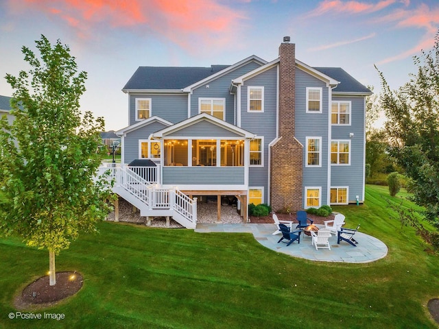 back house at dusk with a yard, a patio area, and a sunroom