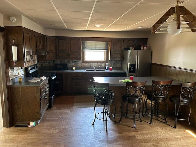 kitchen featuring stainless steel appliances, light wood-type flooring, a kitchen bar, a paneled ceiling, and sink