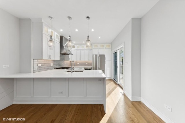 kitchen featuring stainless steel refrigerator, sink, wall chimney exhaust hood, kitchen peninsula, and white cabinets