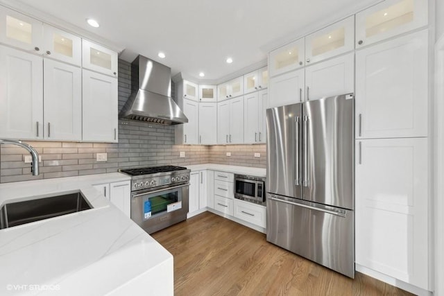 kitchen with appliances with stainless steel finishes, tasteful backsplash, wall chimney exhaust hood, sink, and white cabinetry