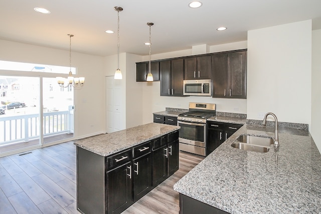 kitchen featuring light hardwood / wood-style floors, light stone countertops, pendant lighting, stainless steel appliances, and sink