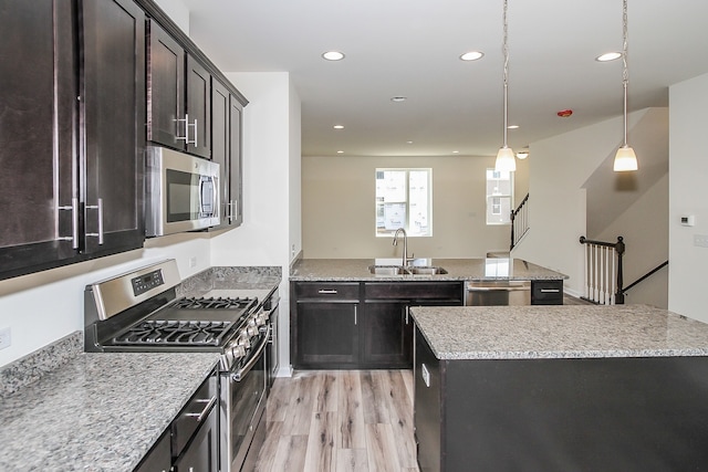 kitchen featuring appliances with stainless steel finishes, hanging light fixtures, light hardwood / wood-style floors, a center island, and sink