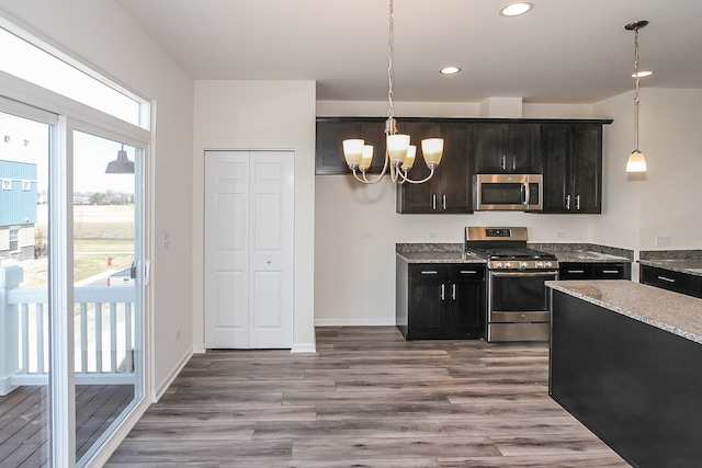 kitchen featuring appliances with stainless steel finishes, hanging light fixtures, light stone counters, light wood-type flooring, and a notable chandelier