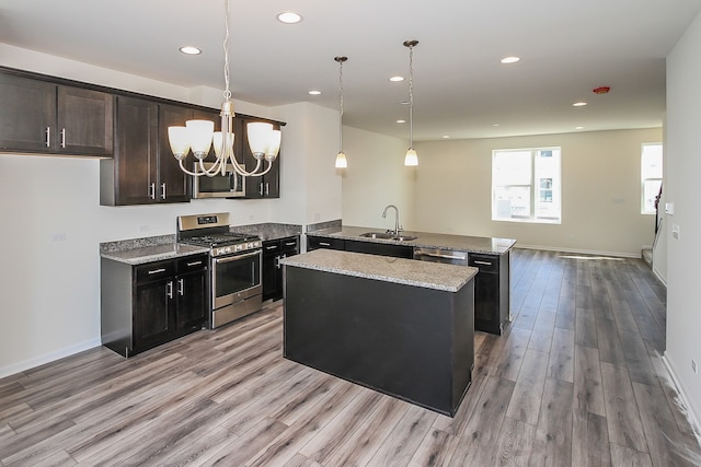 kitchen with light stone counters, light hardwood / wood-style flooring, decorative light fixtures, appliances with stainless steel finishes, and a center island