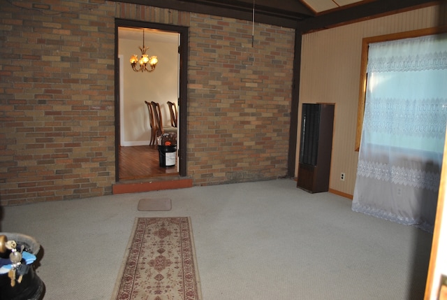 spare room with carpet floors, a chandelier, and brick wall