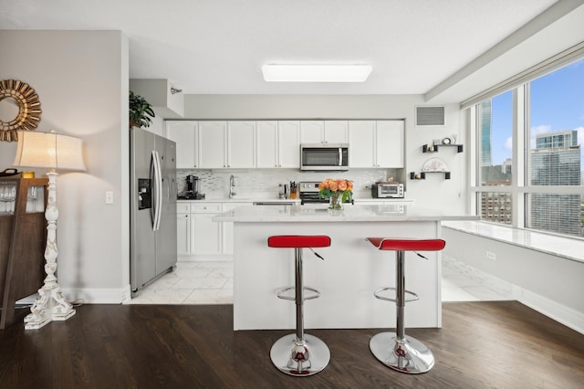 kitchen with appliances with stainless steel finishes, a kitchen breakfast bar, a kitchen island, decorative backsplash, and white cabinets