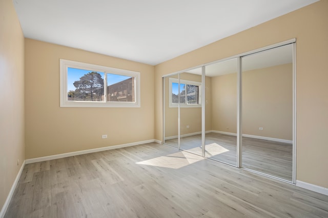 unfurnished bedroom with multiple windows, light hardwood / wood-style flooring, and a closet