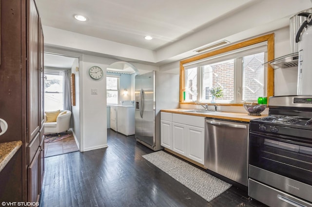 kitchen with washer and dryer, sink, white cabinets, dark hardwood / wood-style flooring, and stainless steel appliances