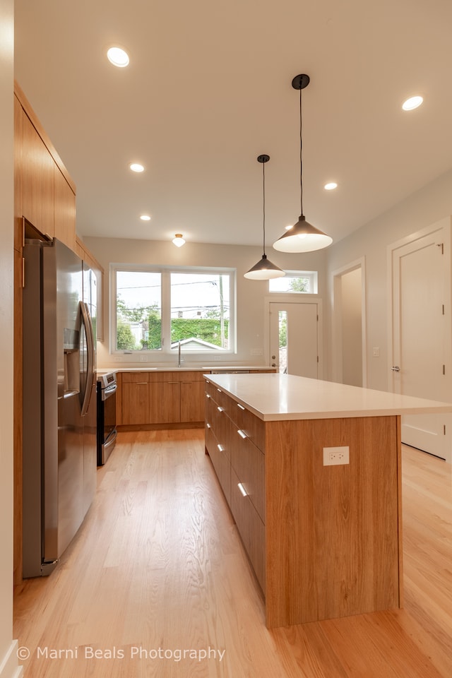 kitchen with decorative light fixtures, appliances with stainless steel finishes, light hardwood / wood-style floors, and a kitchen island