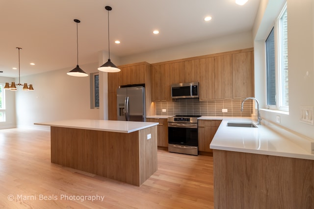 kitchen with pendant lighting, stainless steel appliances, a center island, light hardwood / wood-style flooring, and sink