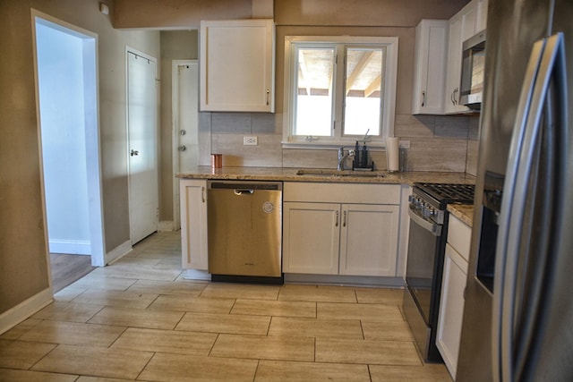 kitchen with stainless steel appliances, white cabinetry, sink, and light stone counters