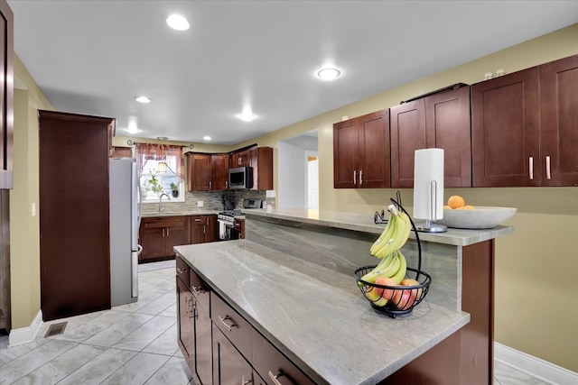 kitchen featuring appliances with stainless steel finishes, light tile patterned flooring, light stone counters, tasteful backsplash, and kitchen peninsula