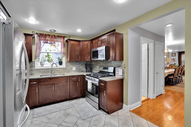 kitchen with sink, decorative light fixtures, backsplash, appliances with stainless steel finishes, and light hardwood / wood-style floors