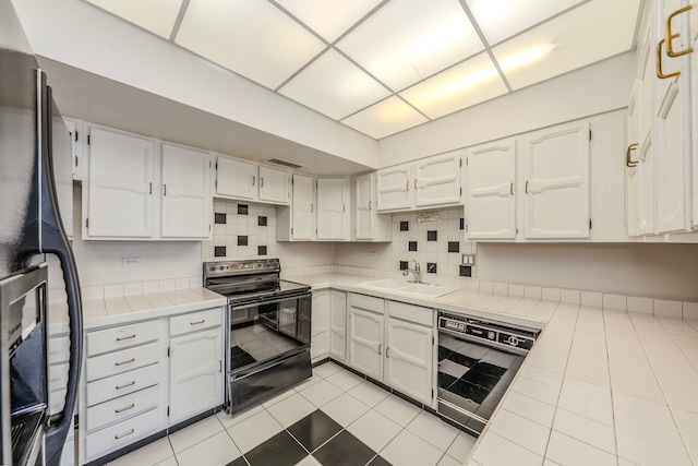 kitchen featuring dishwashing machine, sink, black electric range, white cabinetry, and tile countertops