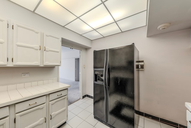 kitchen featuring black fridge, light tile patterned flooring, tile countertops, and white cabinets