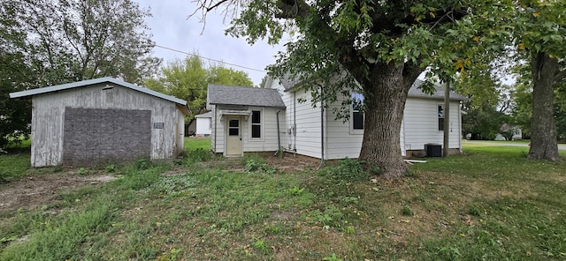 back of house featuring a lawn, an outbuilding, and central AC