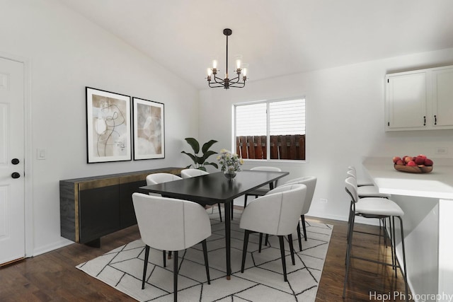 dining area with dark hardwood / wood-style flooring, vaulted ceiling, and an inviting chandelier