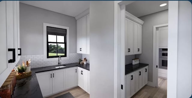 kitchen featuring white cabinets, backsplash, light wood-type flooring, double oven, and sink