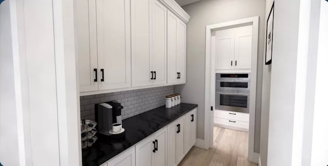 kitchen with double oven, backsplash, white cabinetry, and light hardwood / wood-style flooring