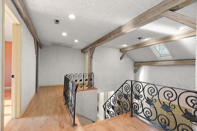 hall with light wood-type flooring, vaulted ceiling with skylight, and a textured ceiling