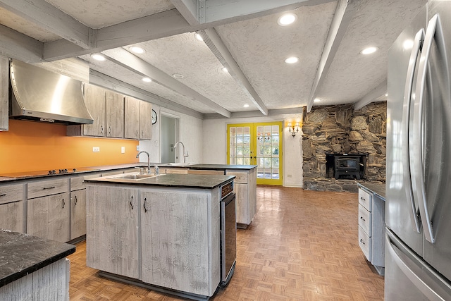 kitchen with stainless steel fridge, beam ceiling, a wood stove, a center island with sink, and extractor fan