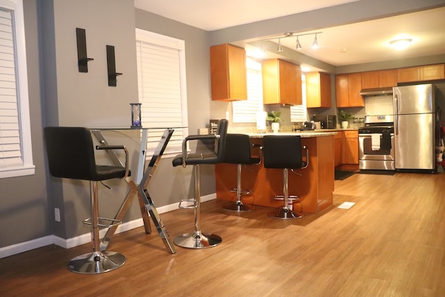 kitchen with light hardwood / wood-style floors, kitchen peninsula, a breakfast bar area, stainless steel appliances, and range hood