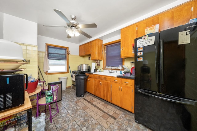 kitchen with tile walls, black appliances, ceiling fan, and sink