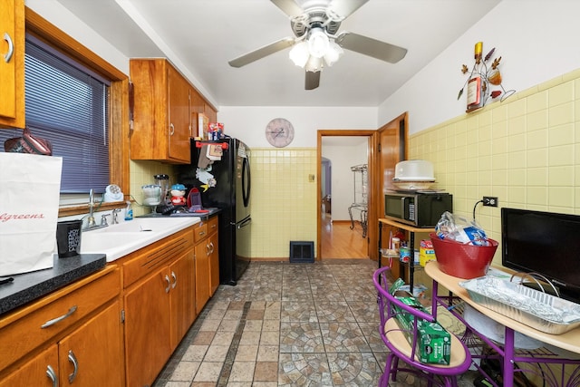 kitchen with tile walls, sink, ceiling fan, and black refrigerator