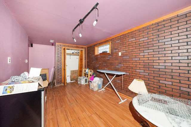 misc room featuring light hardwood / wood-style flooring, brick wall, and rail lighting