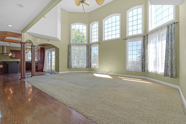 unfurnished living room with wood-type flooring, decorative columns, a towering ceiling, and ceiling fan