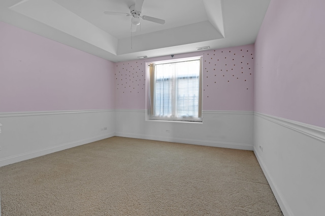 empty room with light carpet, a tray ceiling, and ceiling fan